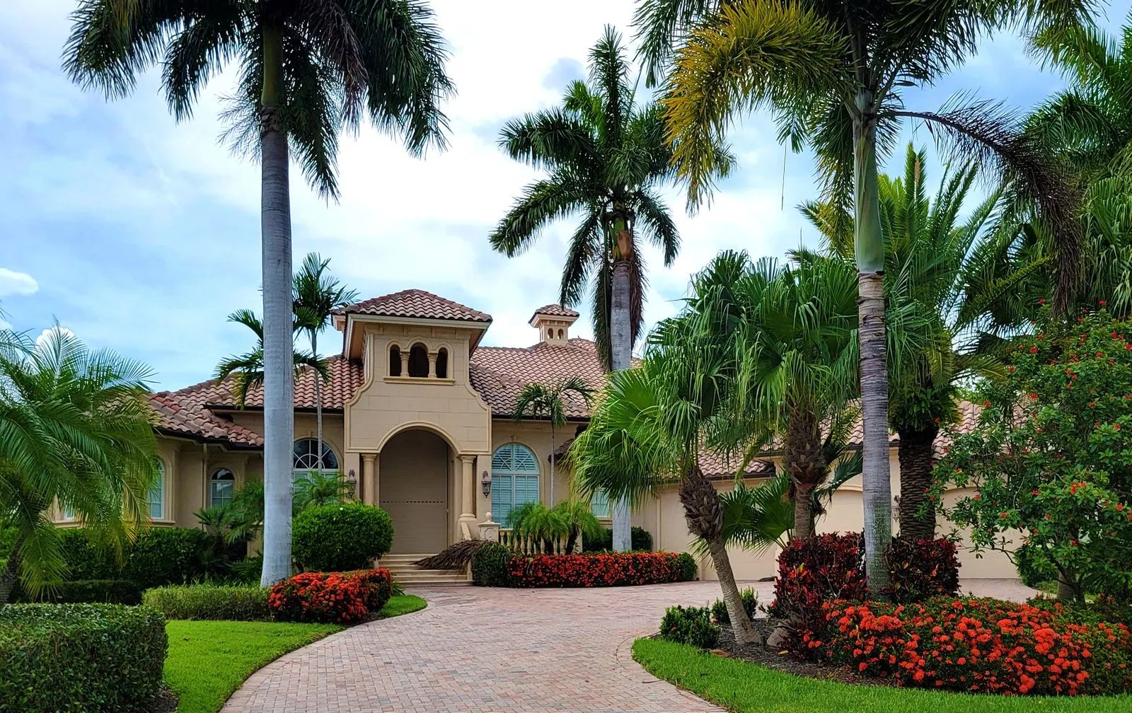 Mediterranean-style Florida estate with a terracotta tile roof, royal palms and a paver driveway