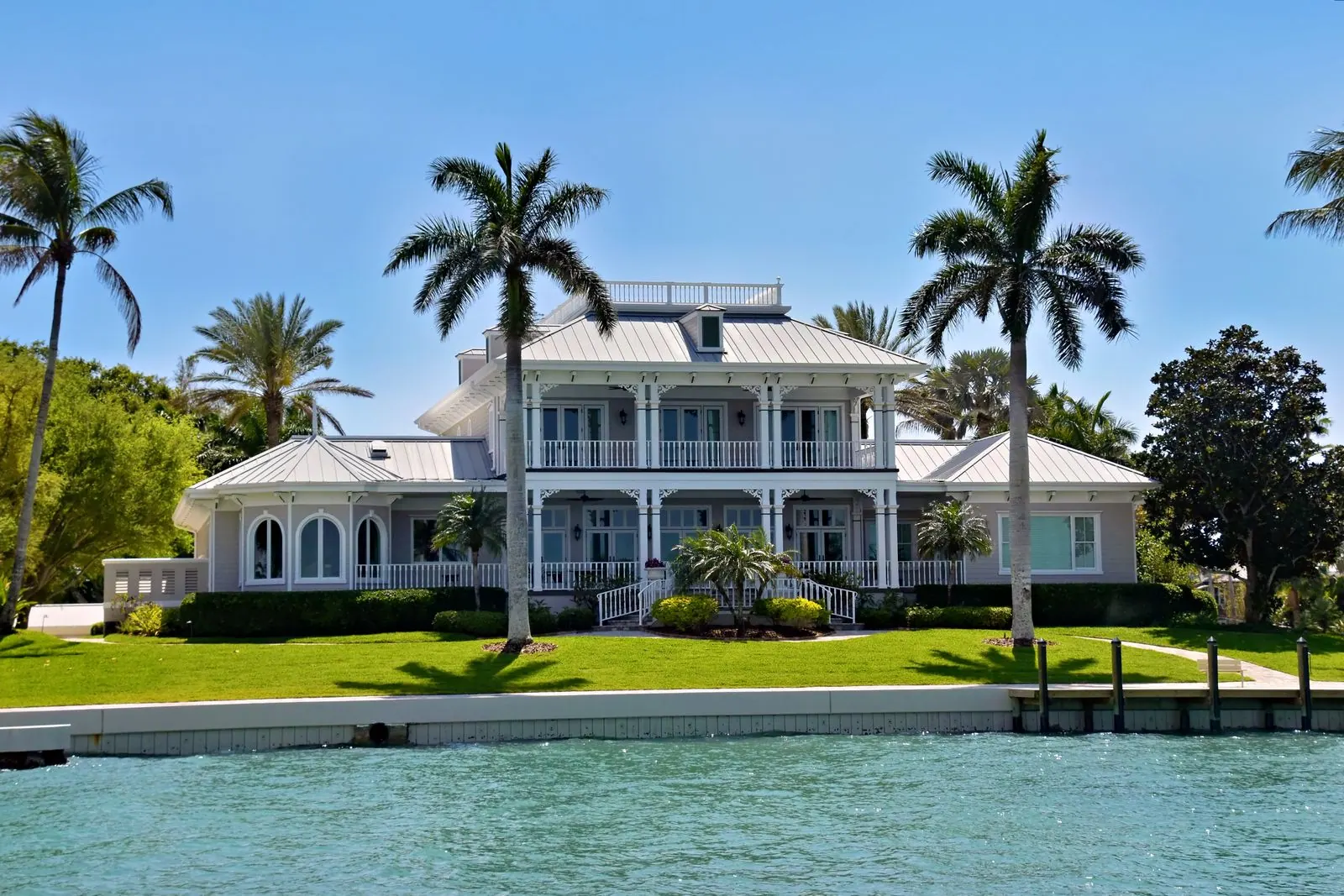 White waterfront estate with green shutters and palms