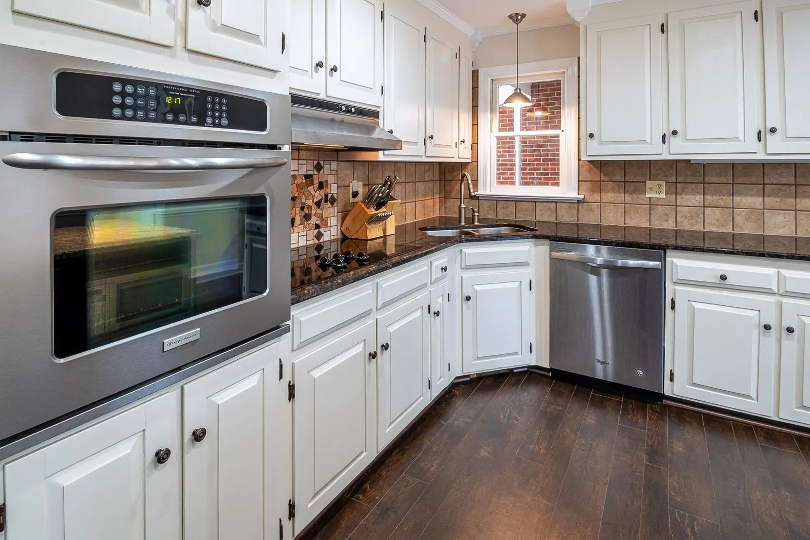 Kitchen with white painted cabinets, dark counters and wood floors