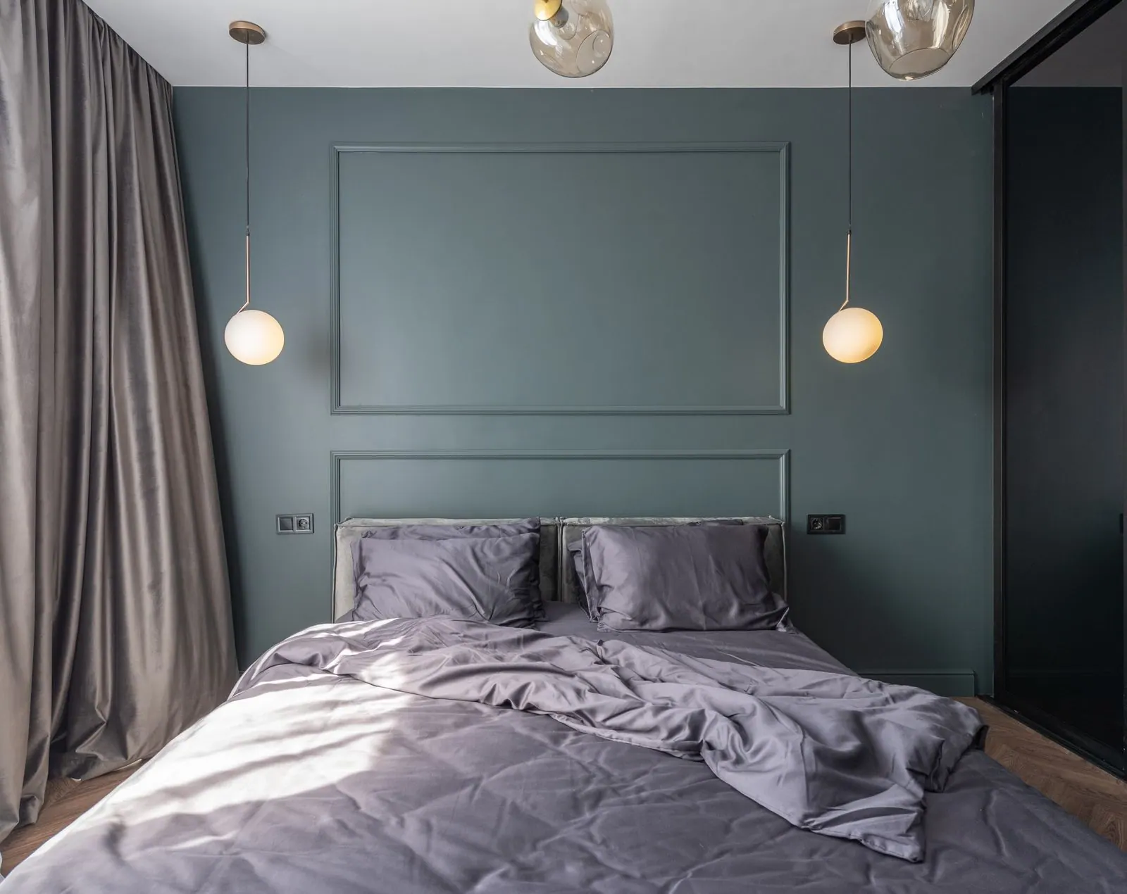 Bedroom with deep blue-green walls, applied wall moulding and brass pendant lights